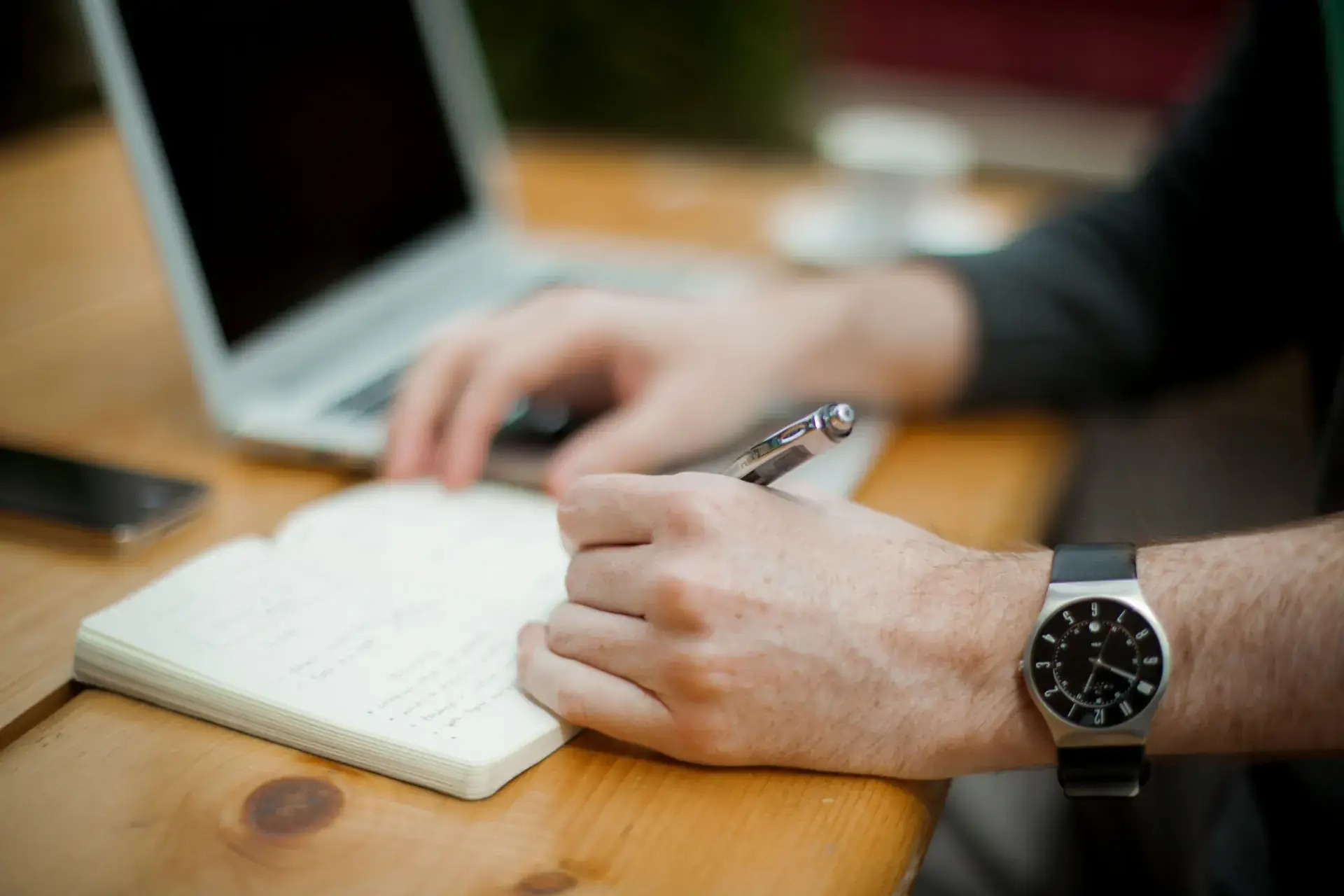 Person writing notes with a laptop